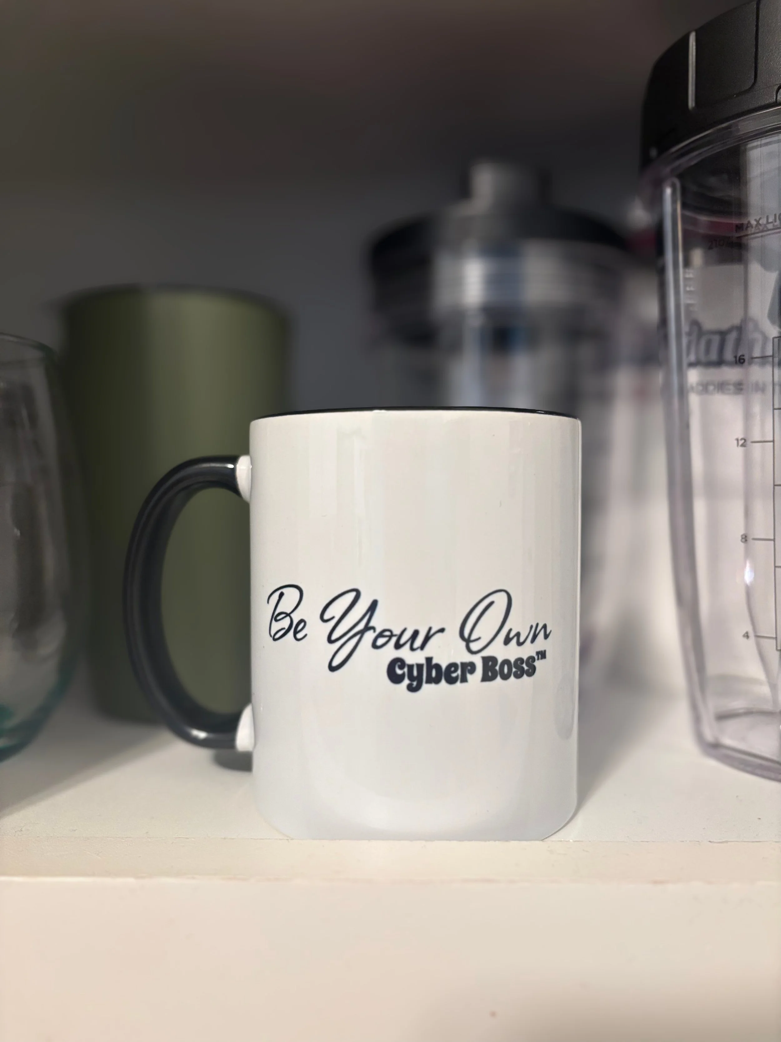 White ceramic mug with black handle and script text reading "Be Your Own Cyber Boss™"