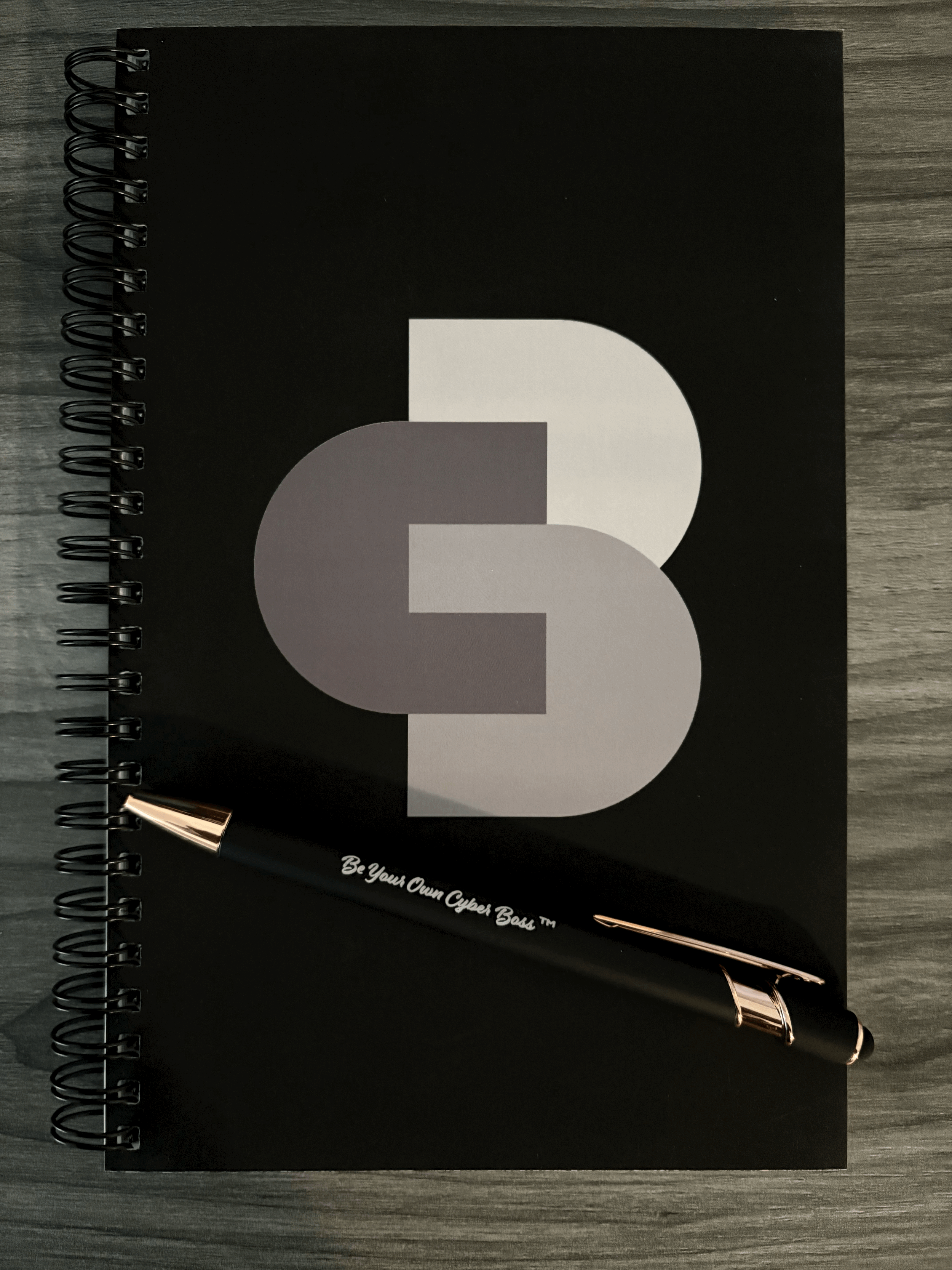 Black Cyber Boss™ notebook with the signature CB logo, styled with a ‘Be Your Own Cyber Boss™’ pen on a neutral background.