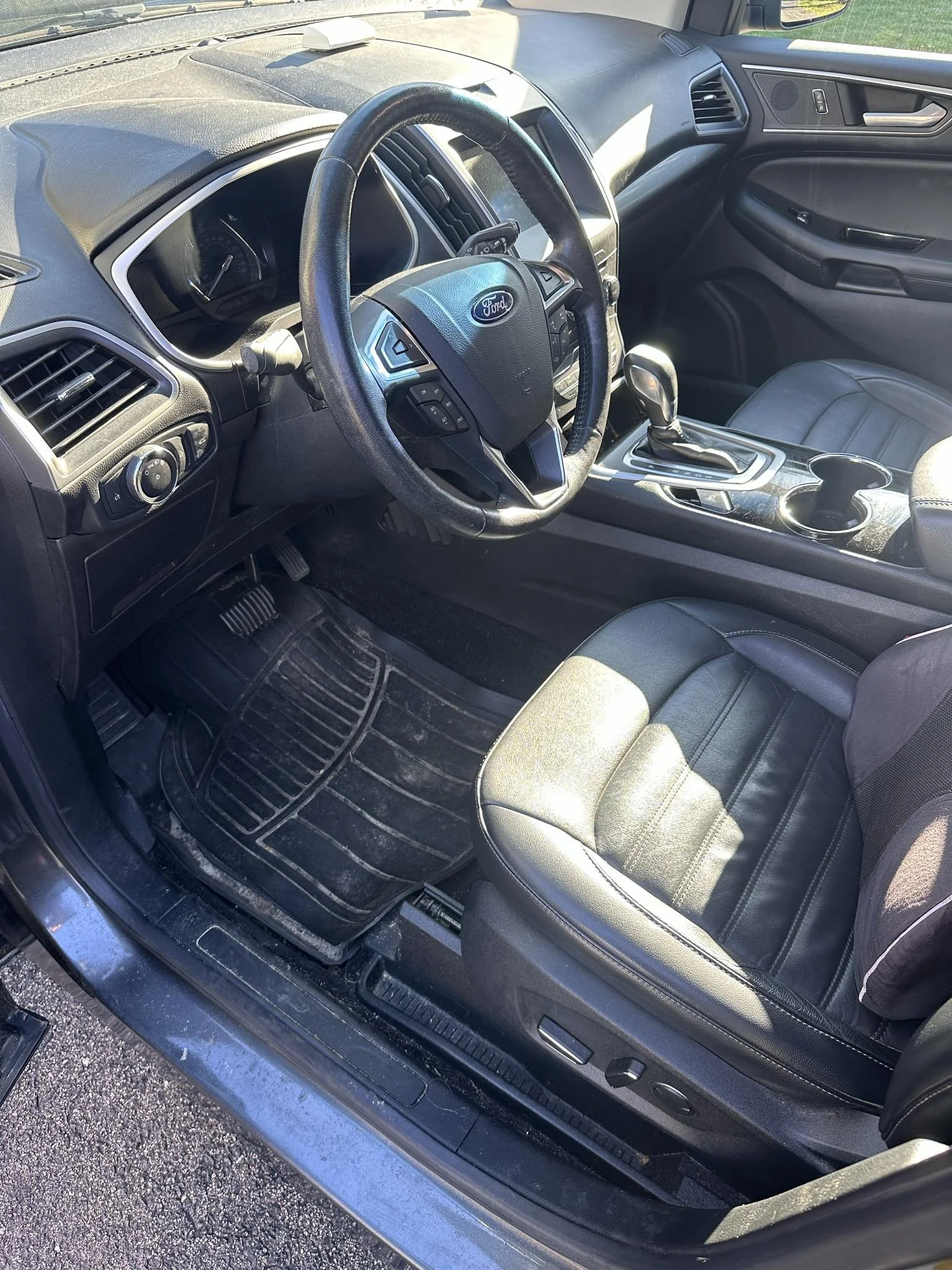 Interior of a Ford car showing the steering wheel, dashboard, center console, and front driver's seat with black leather upholstery.