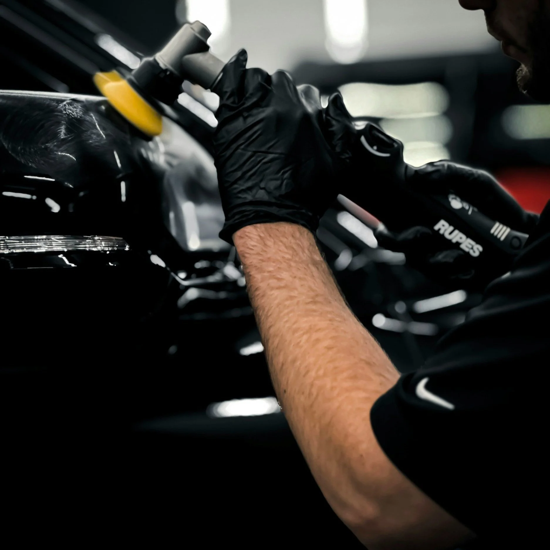 Person polishing a black car with a power polisher and wearing black gloves.