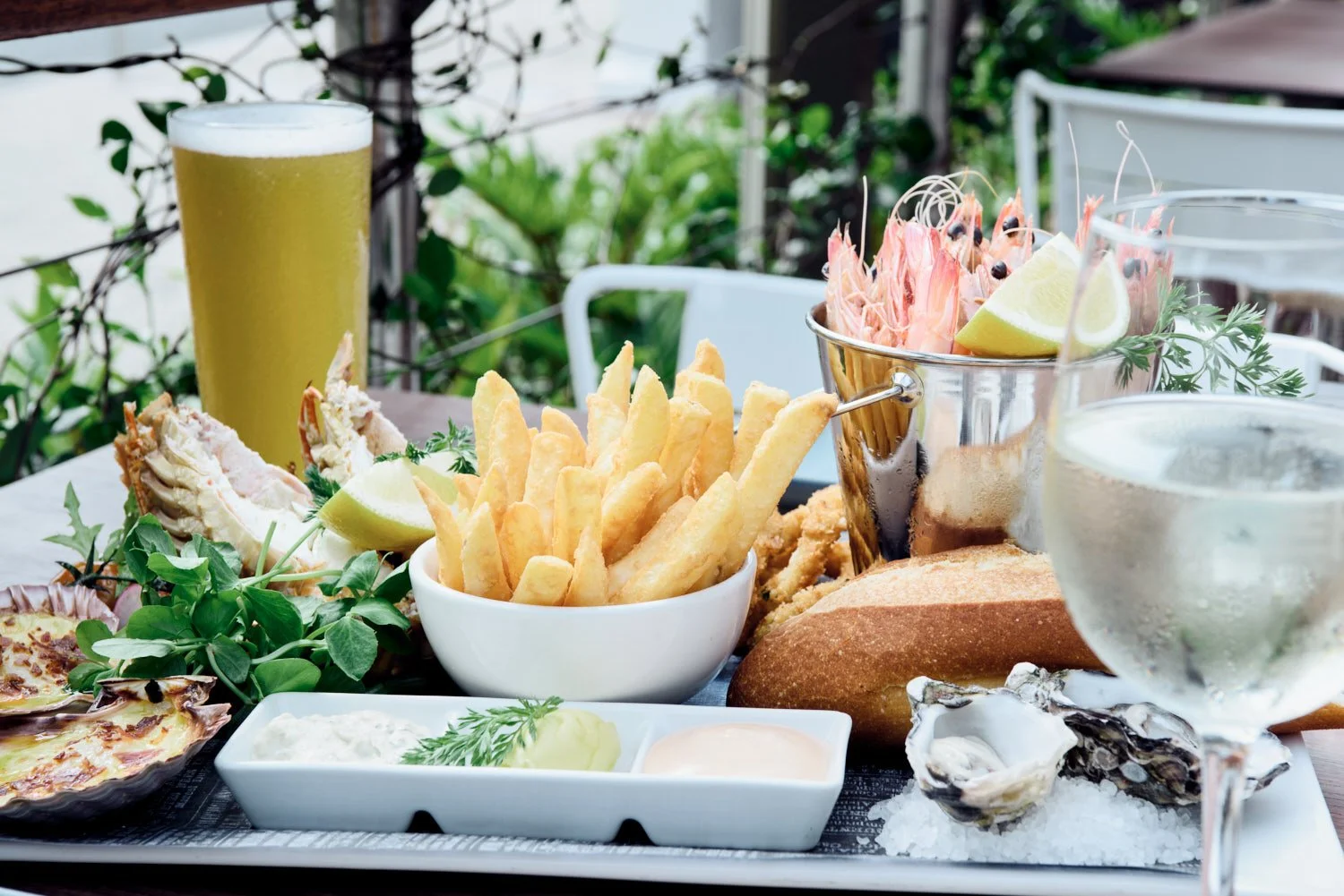 A commercial photograph of a seafood platter with fried fish, French fries, oysters on ice, lobster tail, lemon wedges, and dipping sauces, taken by TomMac photography.