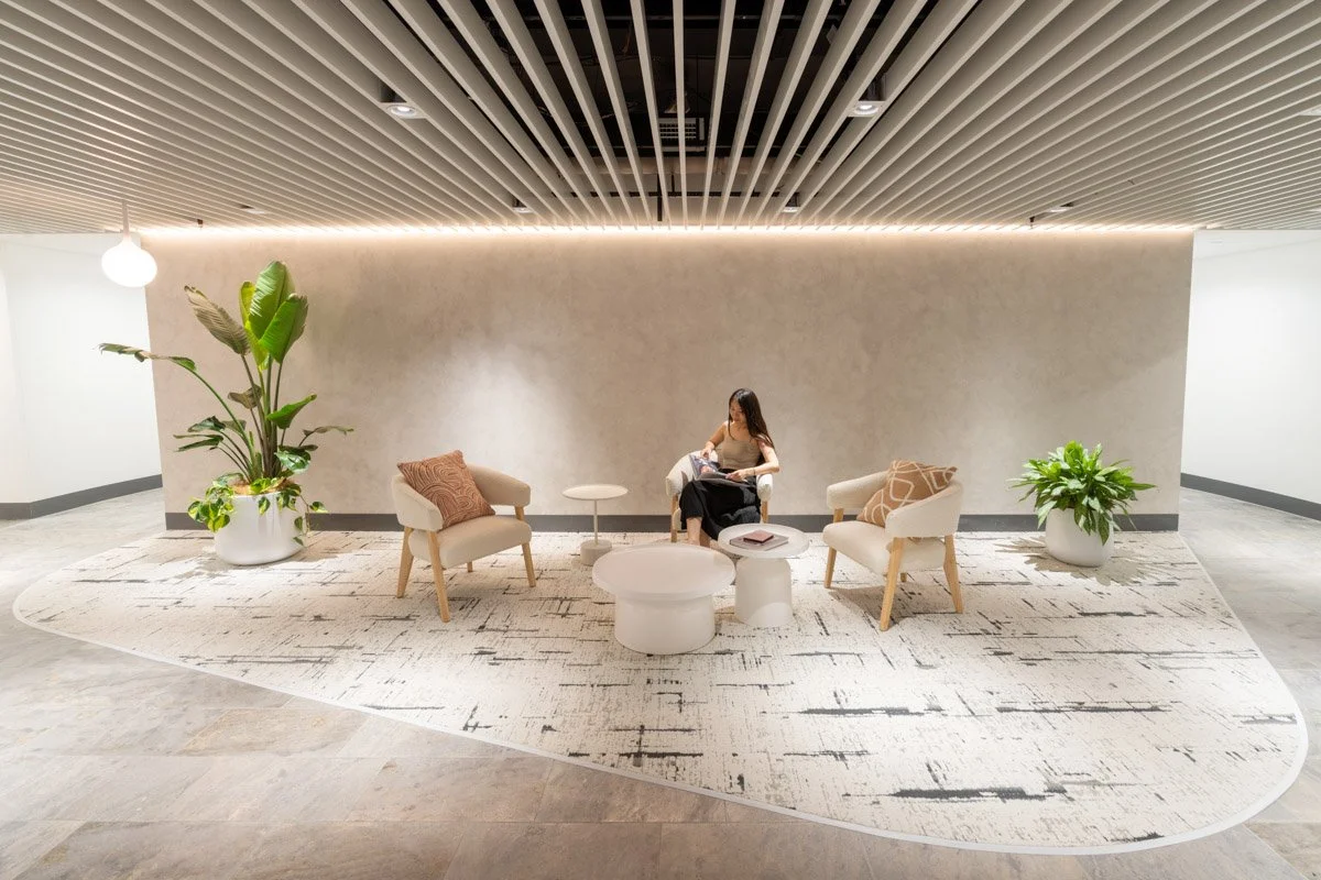 A commercial Interior image of a lounge area with two beige armchairs with pillows, a woman sitting in the middle chair reading a magazine, Taken in Brisbane by Tom MacDonald