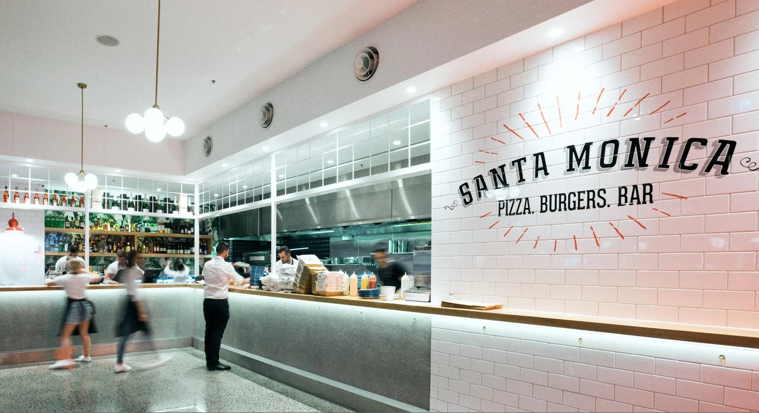 Commercial interior image of Santa Monica Pizza Burgers Bar restaurant with staff working behind the counter and customers in front. tken by Brisbane based commercial photographer Tom MacDonald.