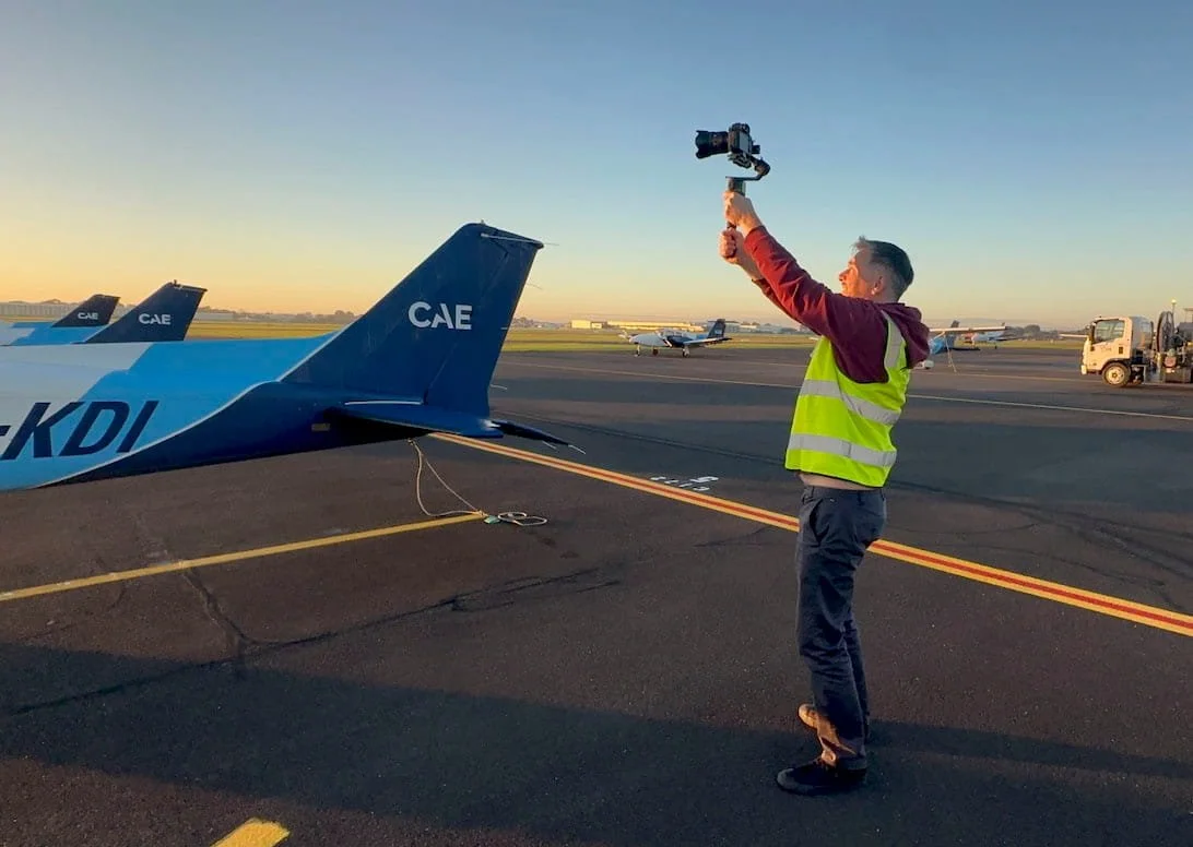 A photograph of Tom MacDonald of TomMac photography, on location at a Melbourne airport shooting video b-roll for a commercial videography project.