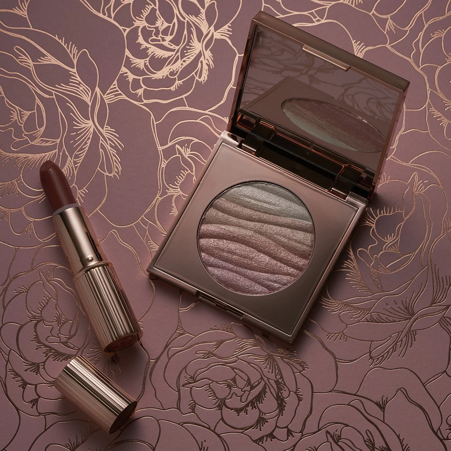 A hero image of a makeup compact with shimmering, pink and metallic shades and a lipstick in a matching metallic tube, placed on a pink floral patterned background. taken by Brisbane based product photographer Tom MacDonald