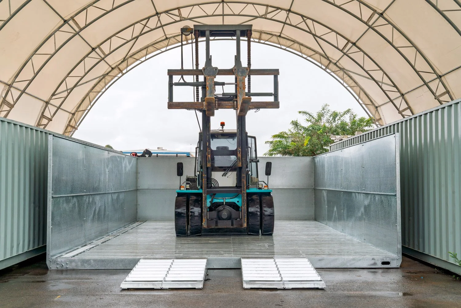  A photograph taken by Brisbane based Tom MacDonald of Tom Mac photography, of a forklift inside a large, semi-enclosed storage area with a curved roof, positioned on a platform with ramps, and surrounded by high walls.