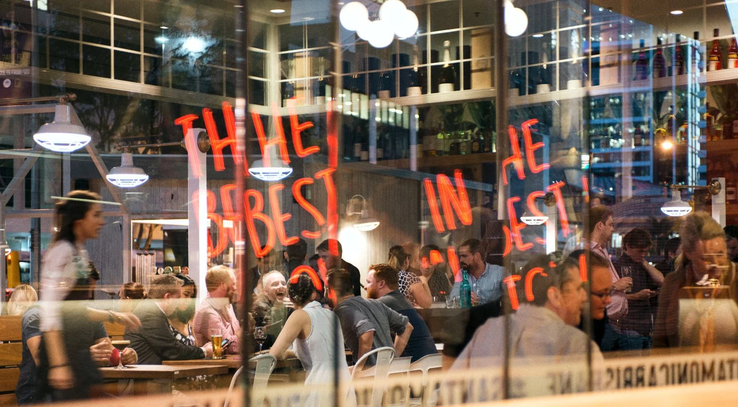 A commercial  photograph of people dining and socializing inside a restaurant seen through a glass window , taken by Brisbane based commercial photographer Tom MacDonald.