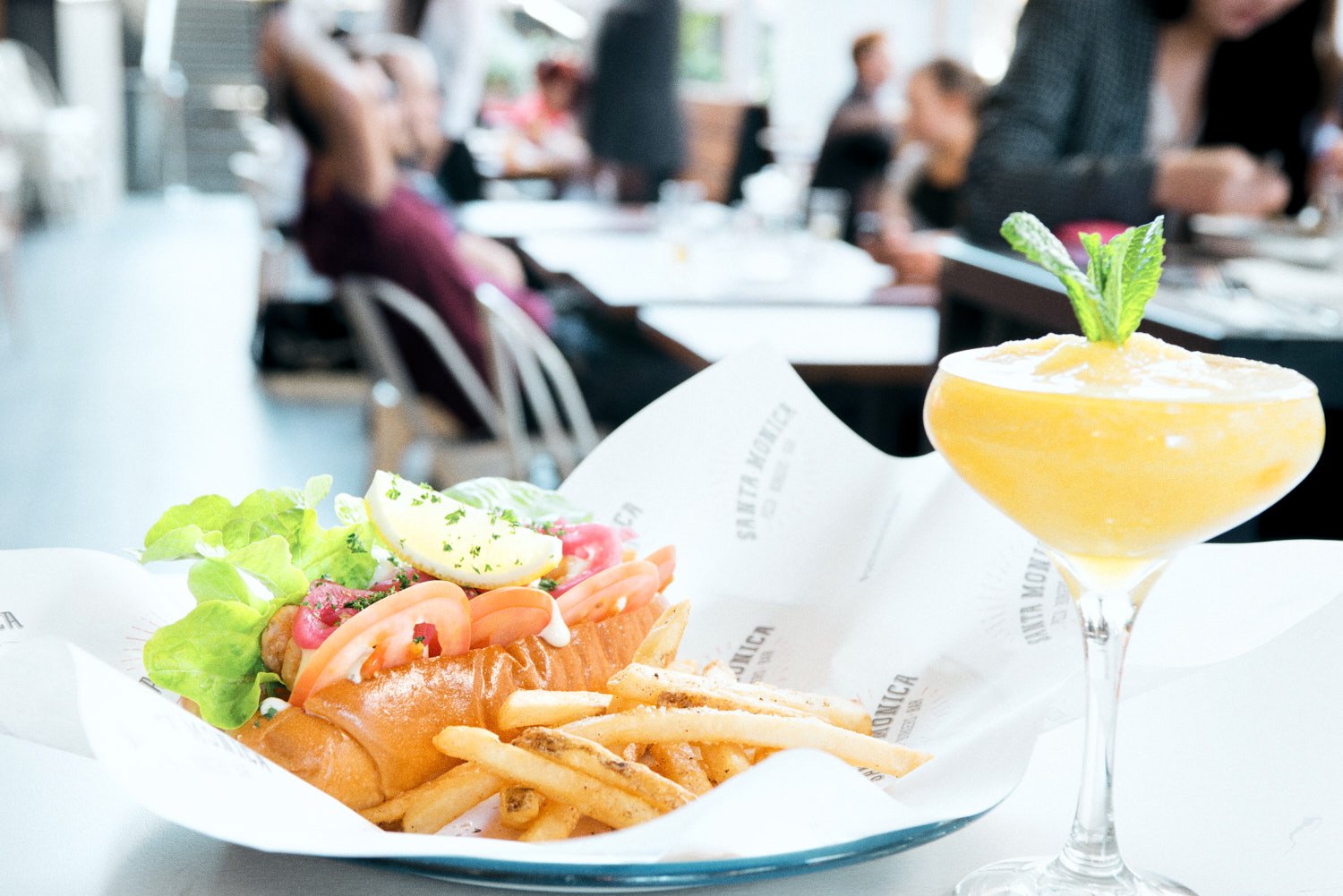 A commercial food photo of a hot dog with lettuce, tomato, lemon wedge, and herbs in a bun with French fries, taken by Tom MacDonald of commercial photography company Tom Mac Photography.