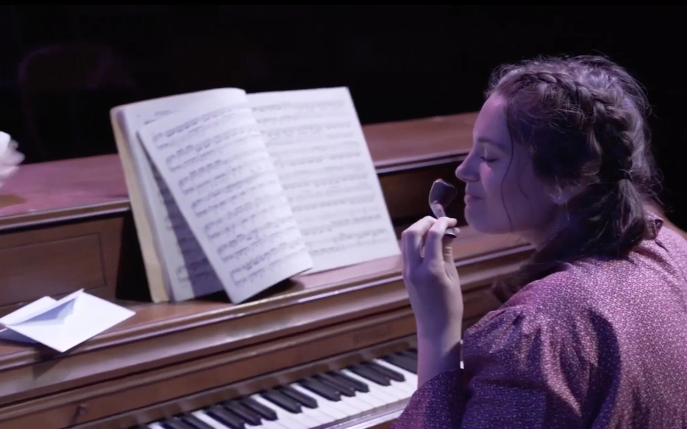 Amy sniffs her father's pipe. On the piano sit a book of sheet music and the letter from Laurie's grandfather.