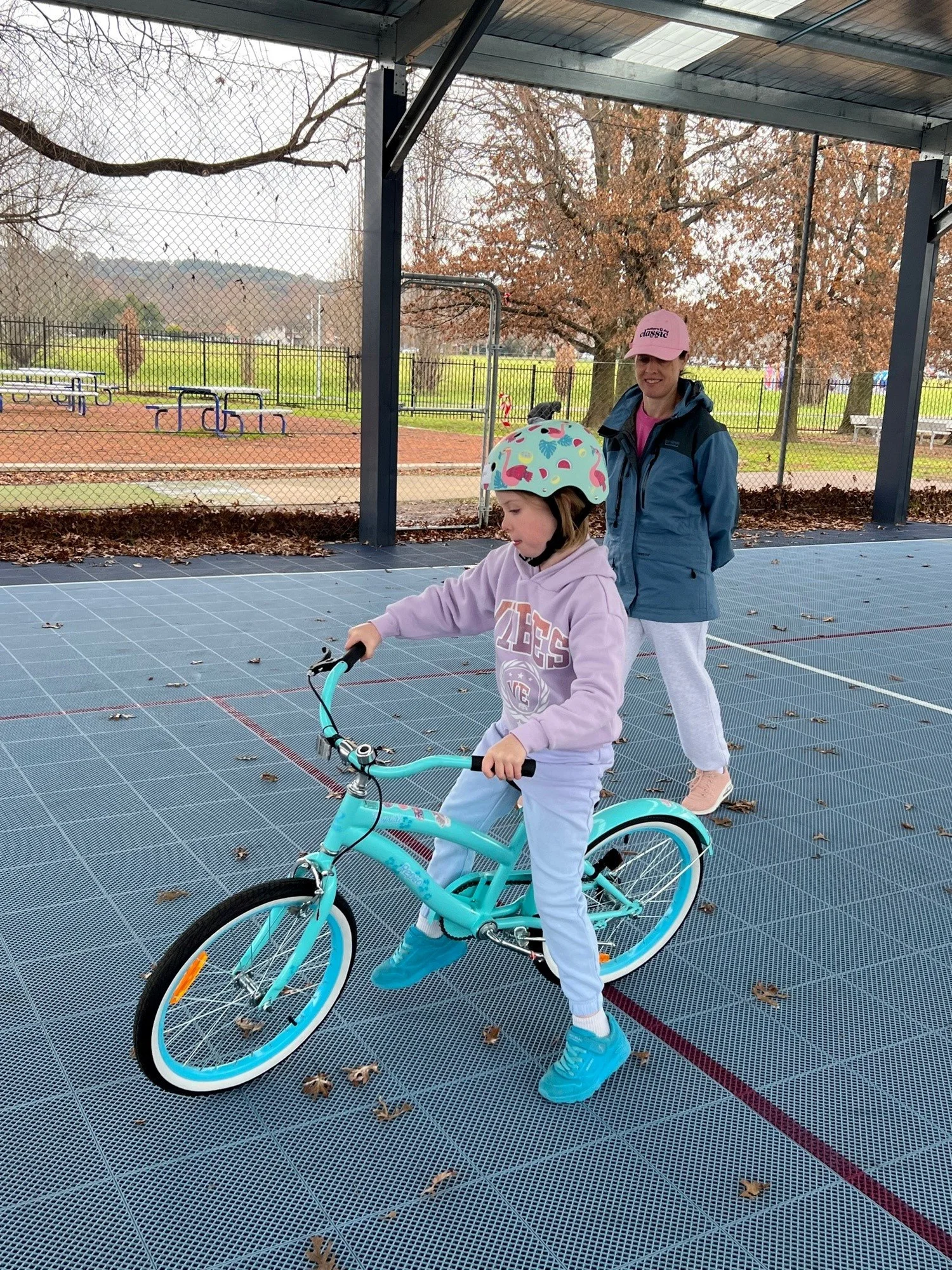 A child practising riding a turquoise bike while her grown-up walks alongside
