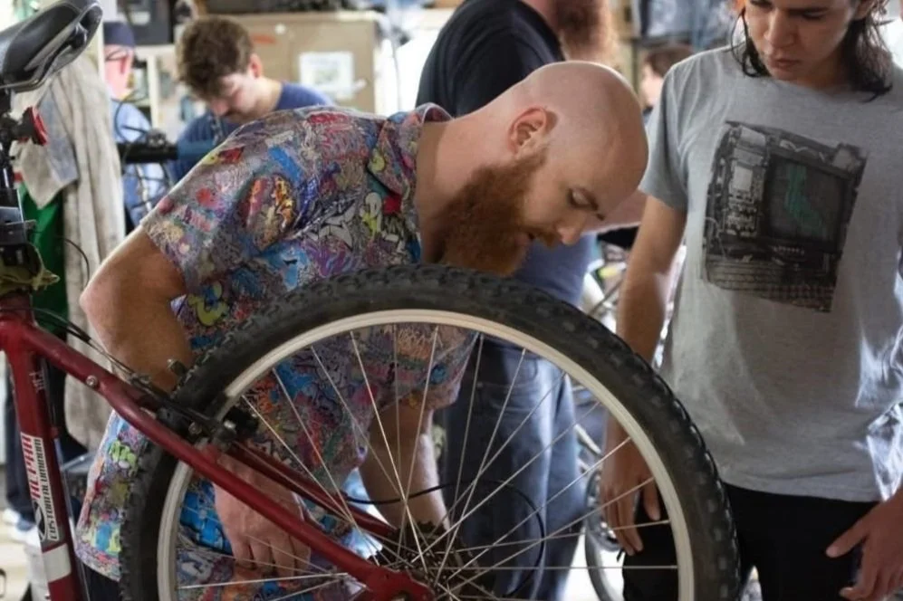 An instructor and participant examining a bicycle wheel during a Pedal Power maintenance workshop