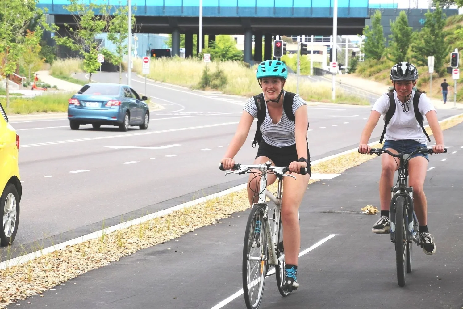 Two helmeted riders cycling on a separated Canberra bike path