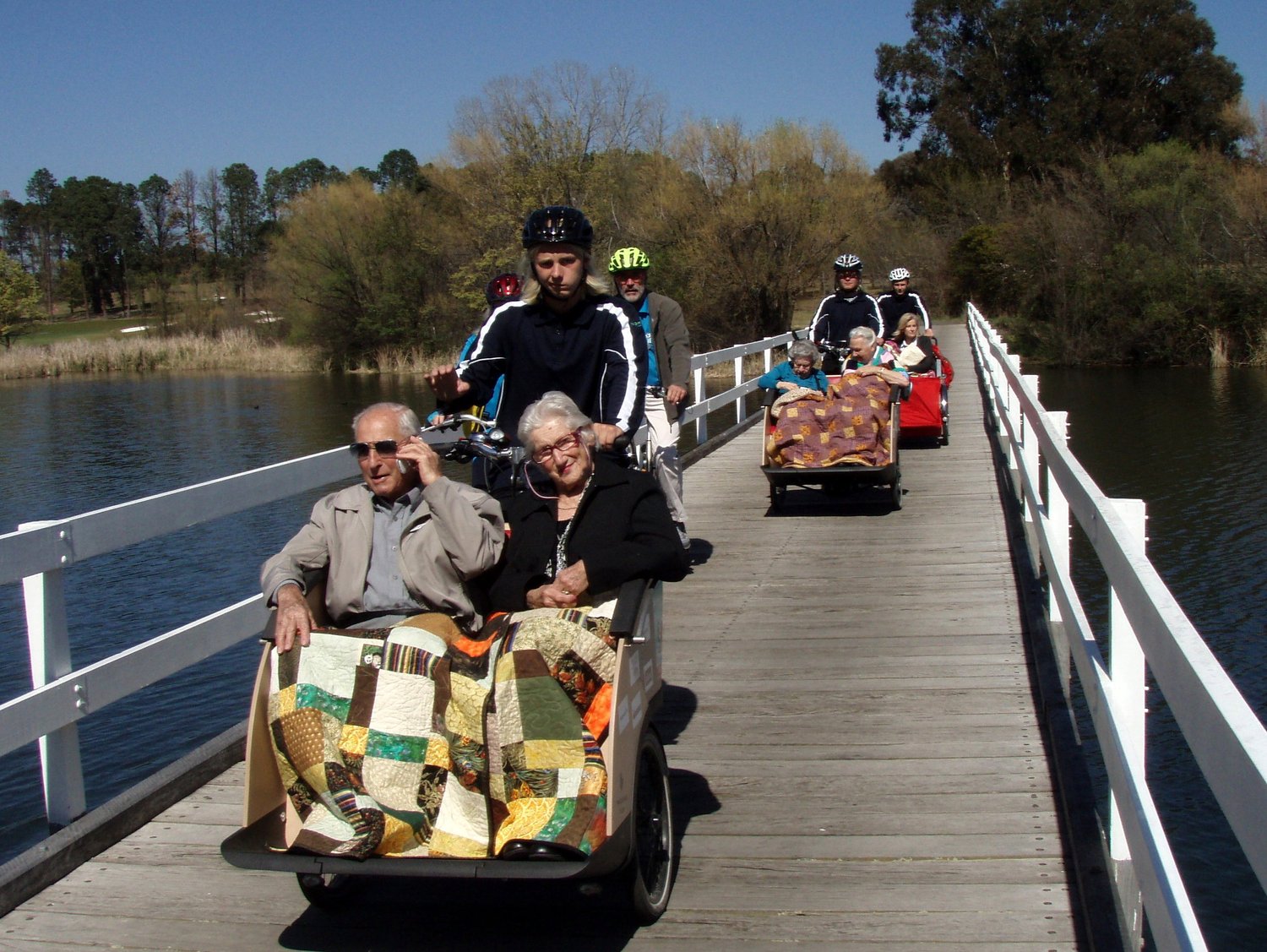 Several trishaws crossing a bridge with passengers and volunteer pilots