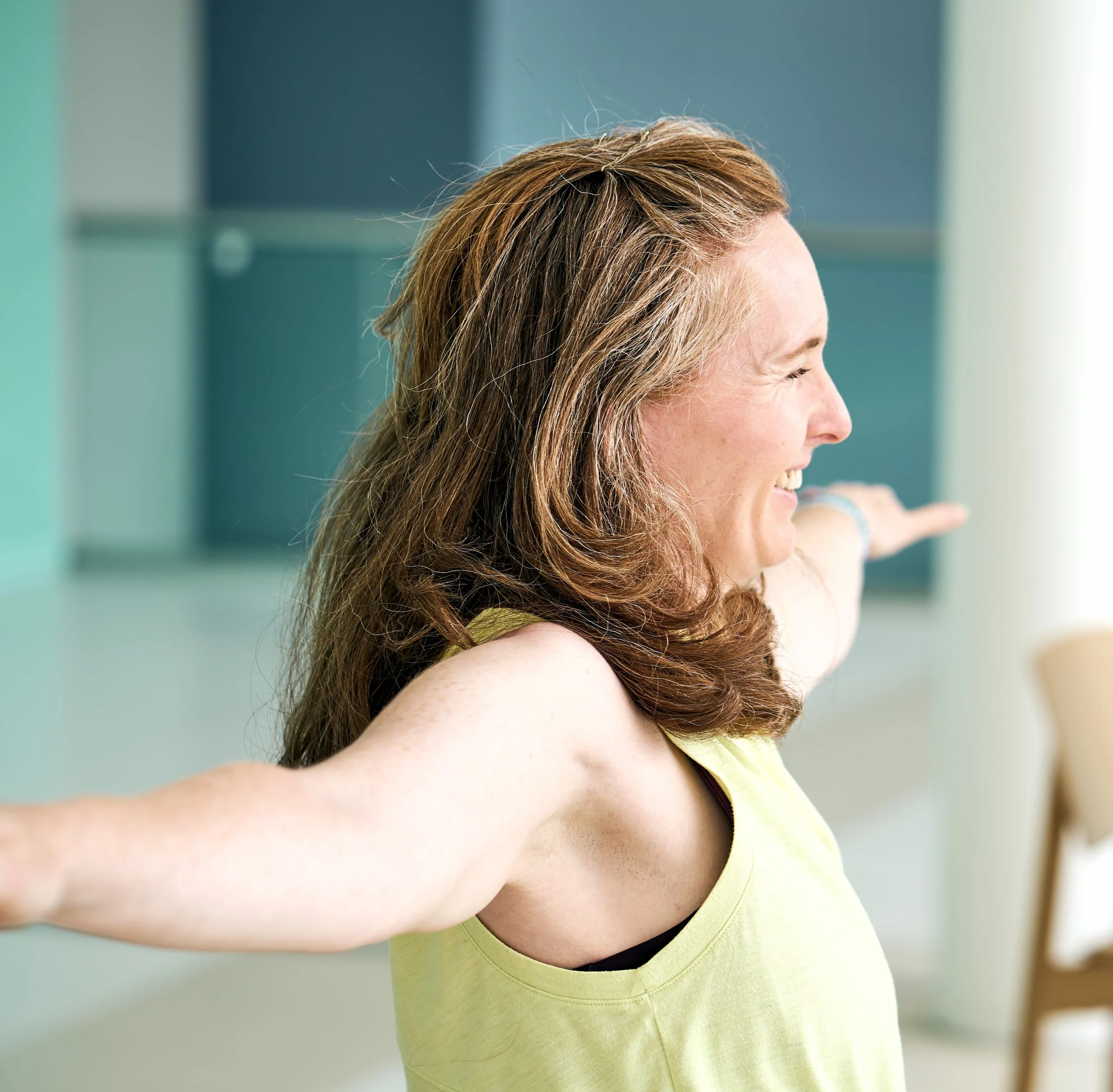 Tula Yoga Jo smiling and stretching her arms out to the sides in a bright, modern room.
