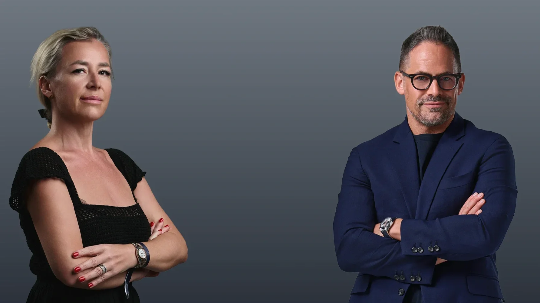 A woman with blonde hair, wearing a black dress, standing with arms crossed, and a man with dark hair, glasses, wearing a navy blazer, standing with arms crossed against a gray background.