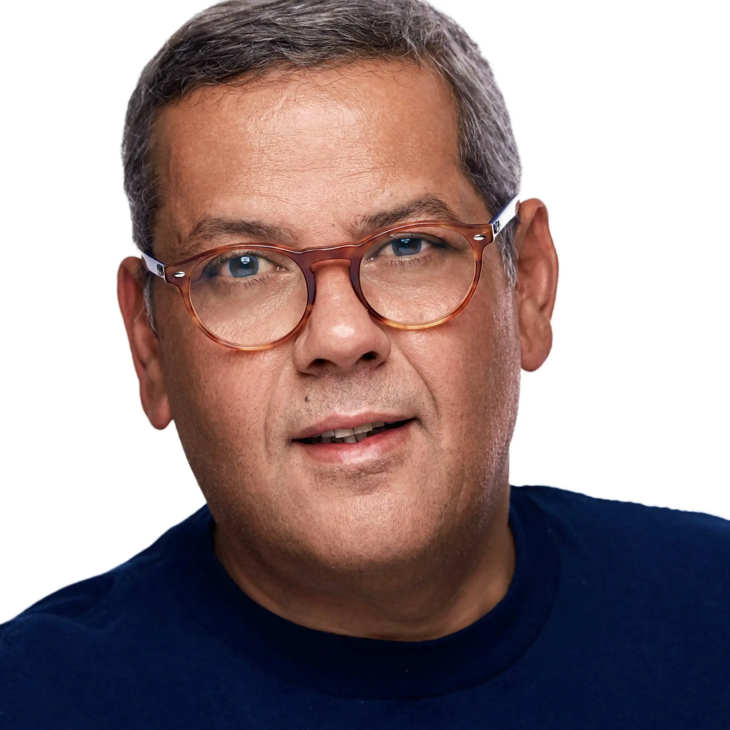 Close-up of a man wearing round glasses, with visible gray hair, wearing a dark blue shirt, and smiling slightly.