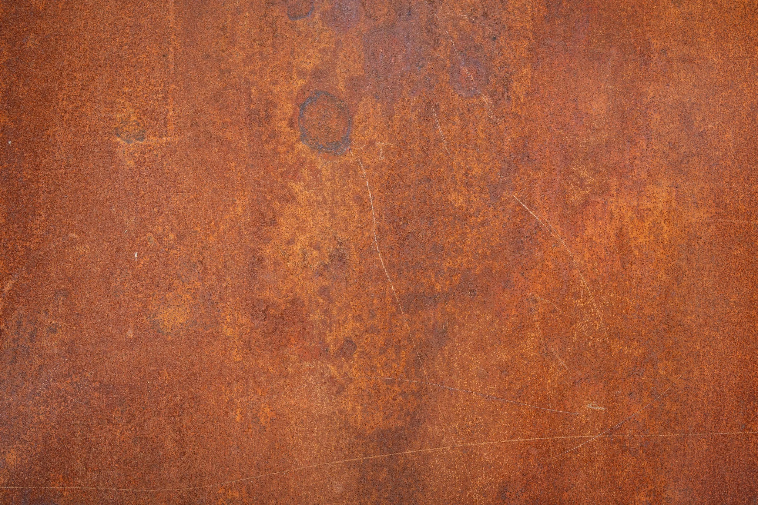 Close-up of a rusty metal surface with a textured, reddish-brown appearance, showing scratches and discoloration.