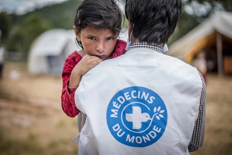 Un docteur de médecins du monde qui porte le gilet de l'ONG a dans ses bras une petite fille népalaise qui a l'air fatiguée