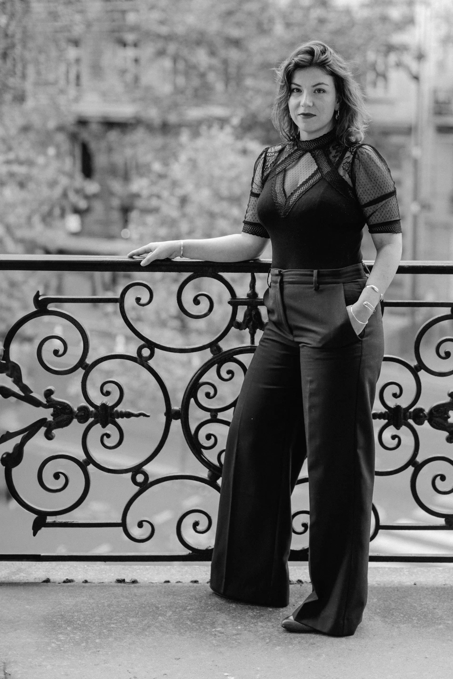 Femme posant près d'une balustrade en fer forgé, en extérieur, en noir et blanc.