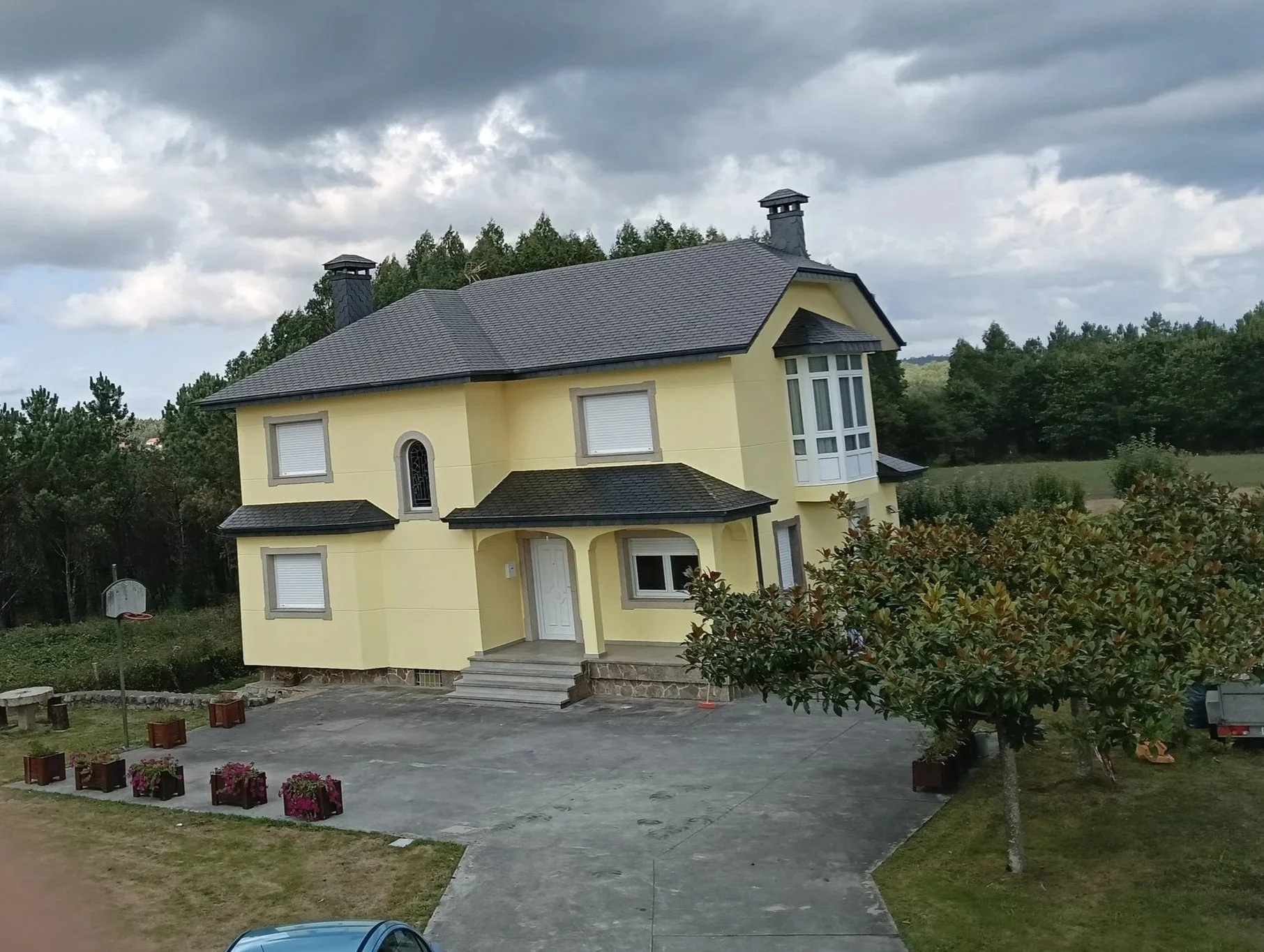 Casa amarilla con tejado negro y persianas blancas.