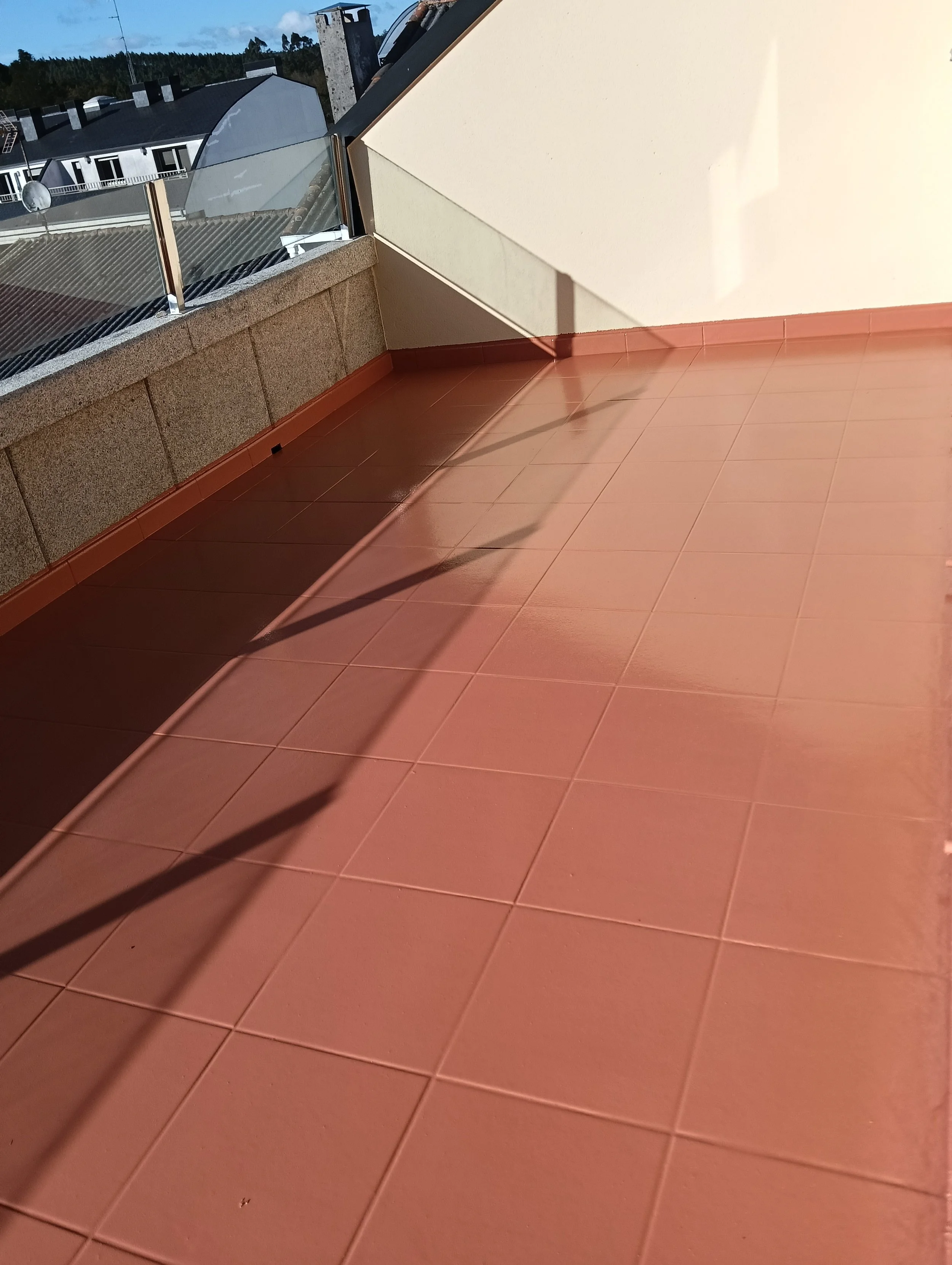 Terraza de suelo color teja, paredes amarillas y frente con piedra y barandilla acristalada. 