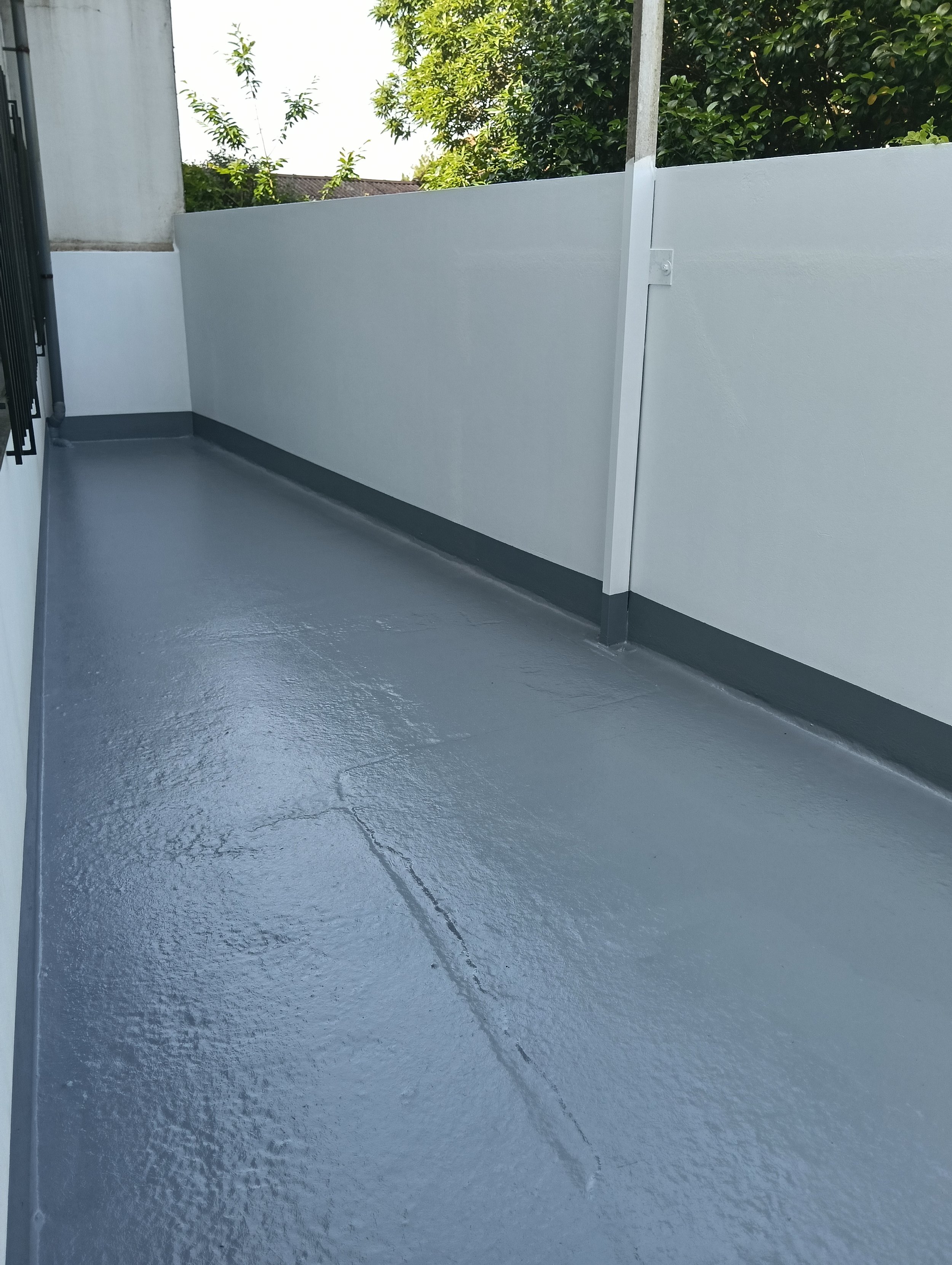 Terraza de suelo gris y paredes blancas con arbol al fondo. 