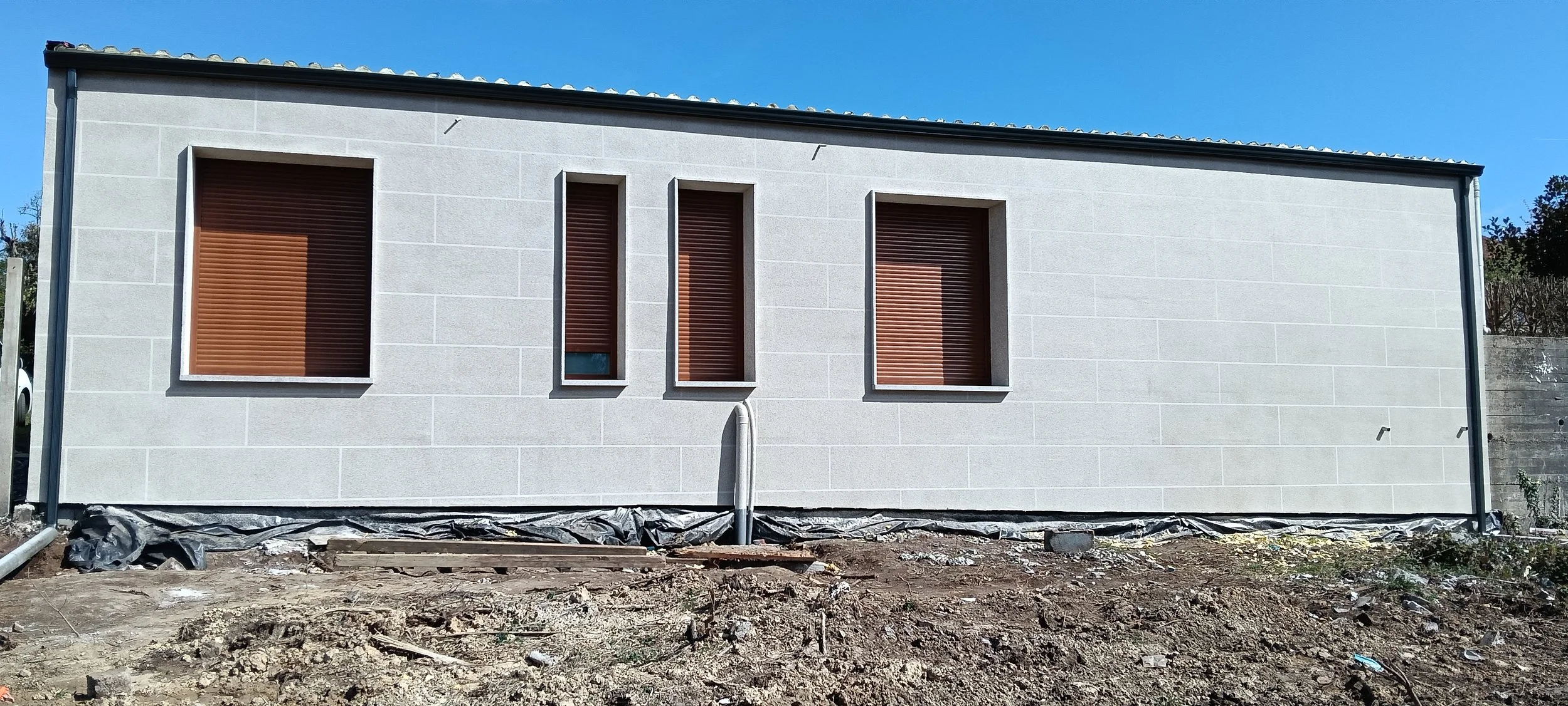 Fachada trasera con pared imitación a piedra y ventanas marrones. 