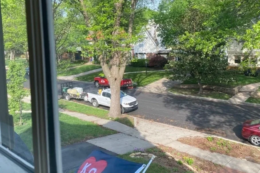 Side-by-side lawn company trucks spraying lawns on a residential street.