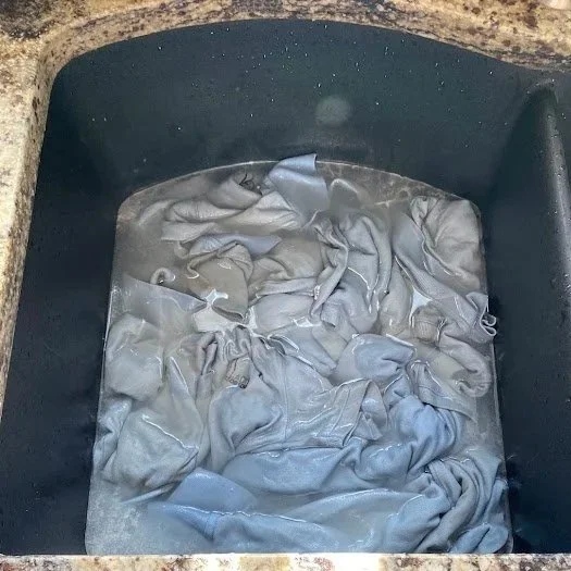 Stained clothing soaking in a kitchen sink.