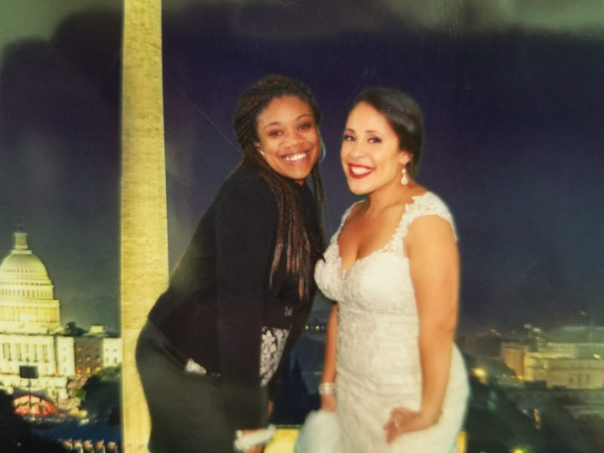 Two women smiling in front of a backdrop featuring the Washington Monument and the U.S. Capitol Building at night.