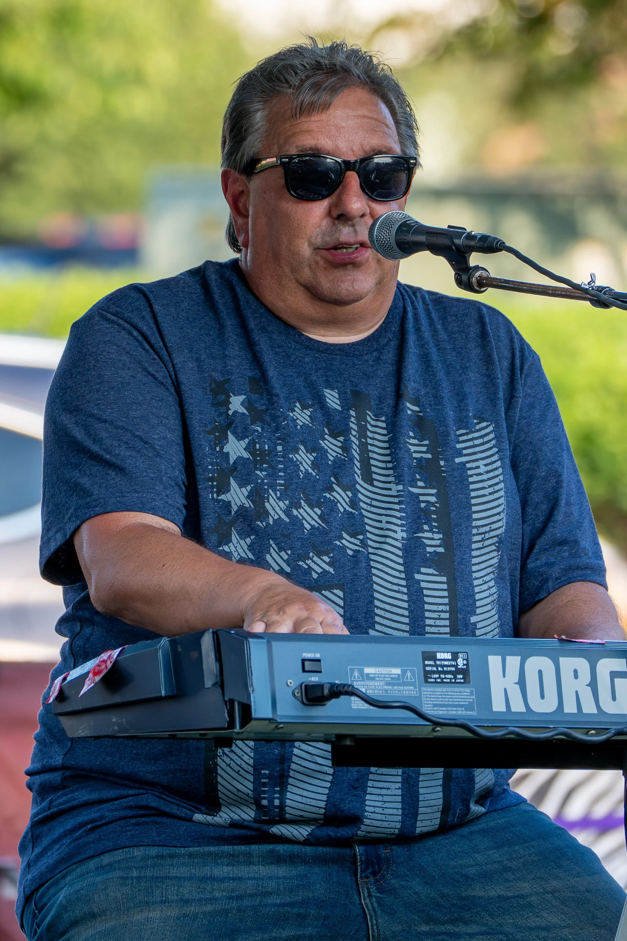 A man wearing sunglasses playing a keyboard at an outdoor event.