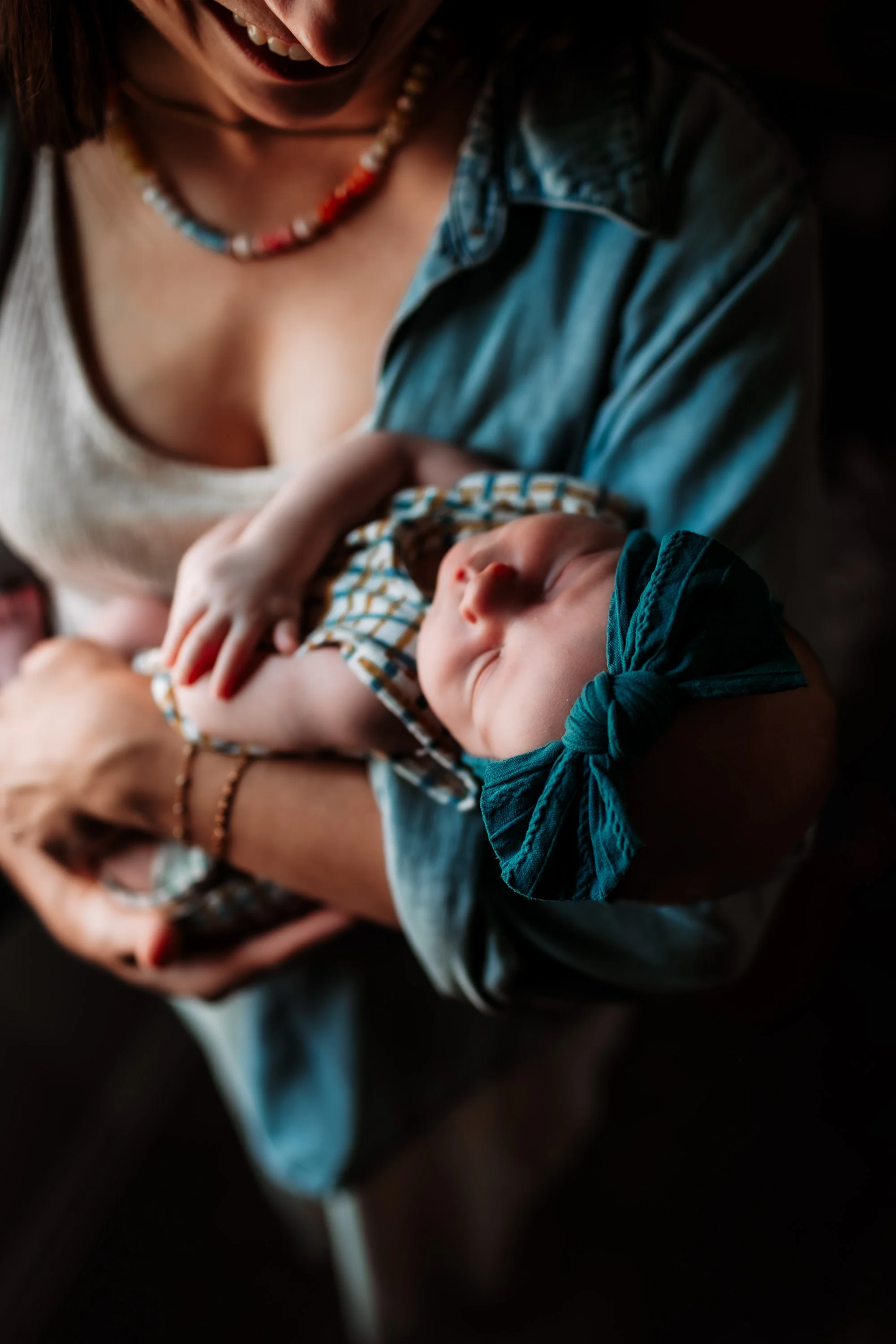 A woman holding a sleeping baby in her arms, both wearing casual clothing and the woman wearing a beaded necklace.