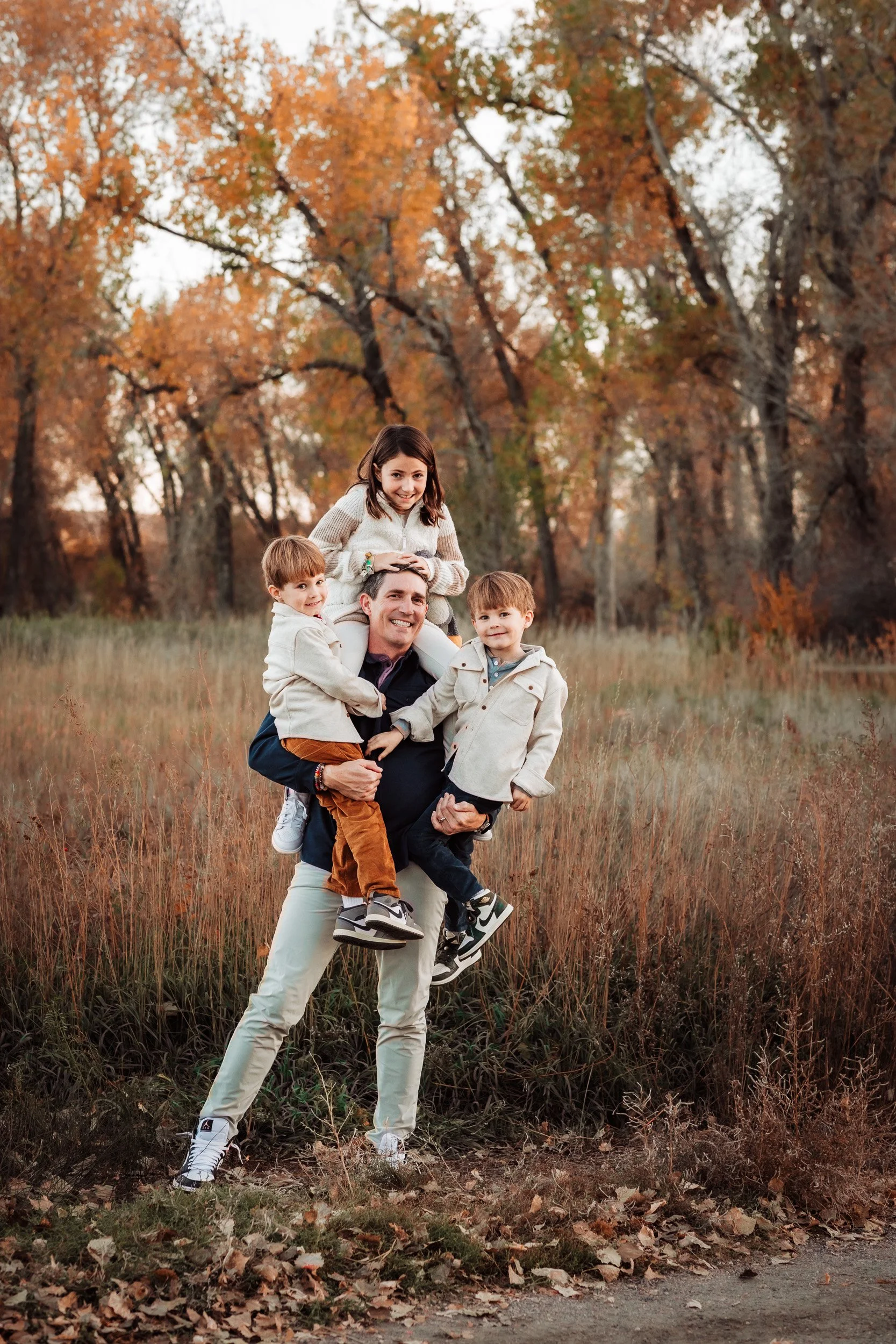 dad holding twin boys and daughter on shoulders in field during golden hour