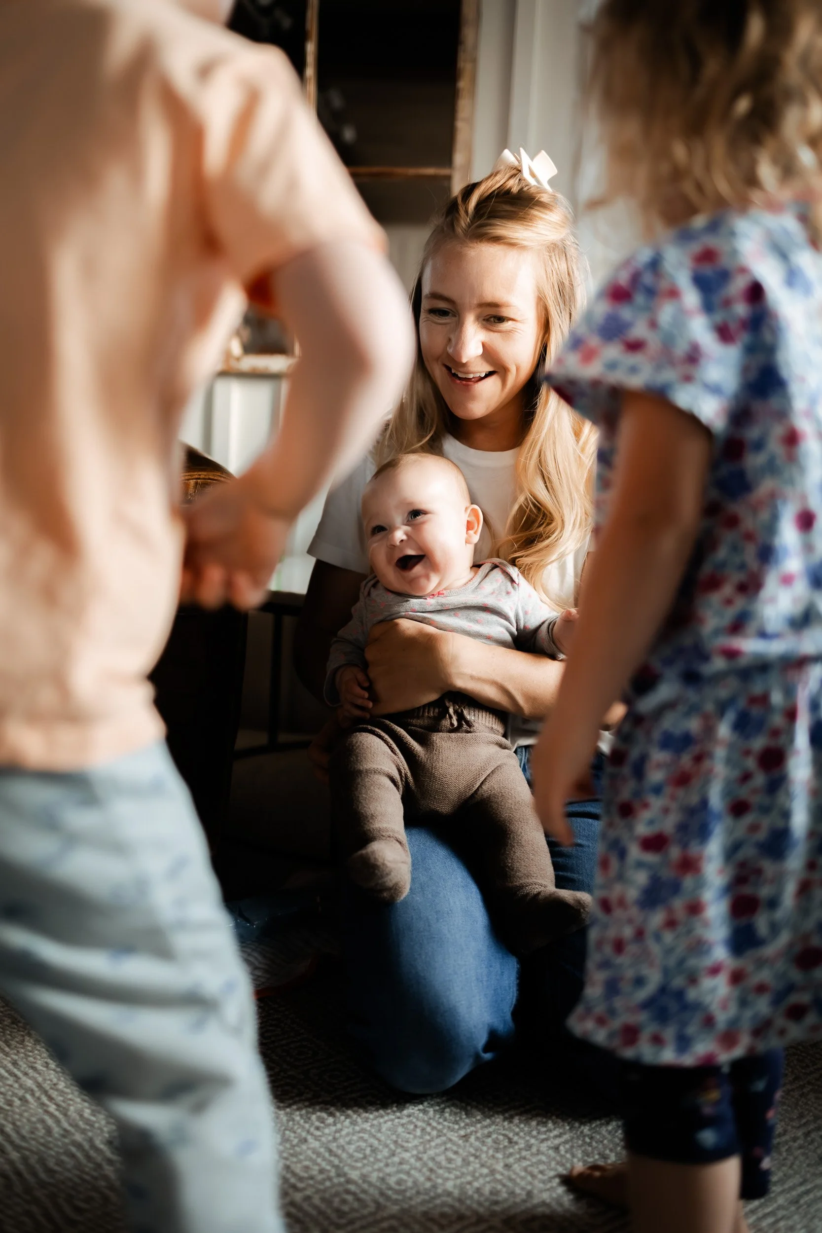 Mother holding her newborn while siblings play nearby during an in-home family session in Boulder