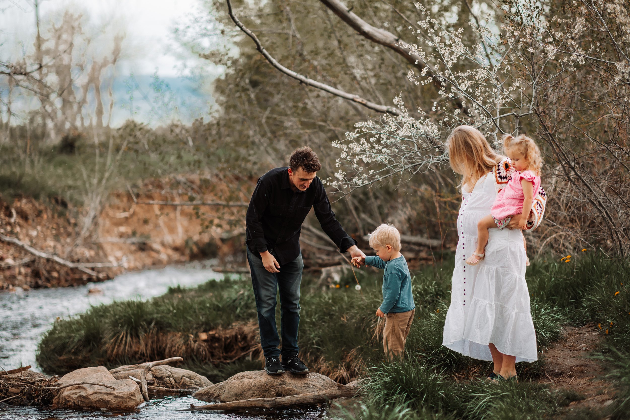 Parents and two children crossing creek along Bobolink Trail during a family maternity session in Boulder, CO