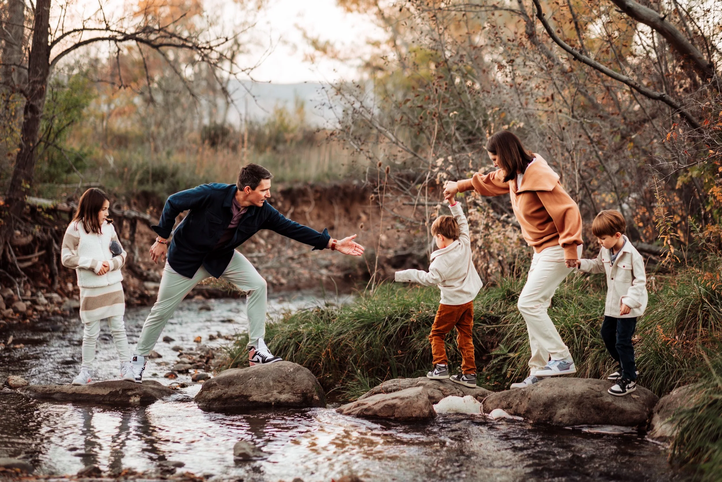 Parents and children crossing the creek during fall family photos in Boulder