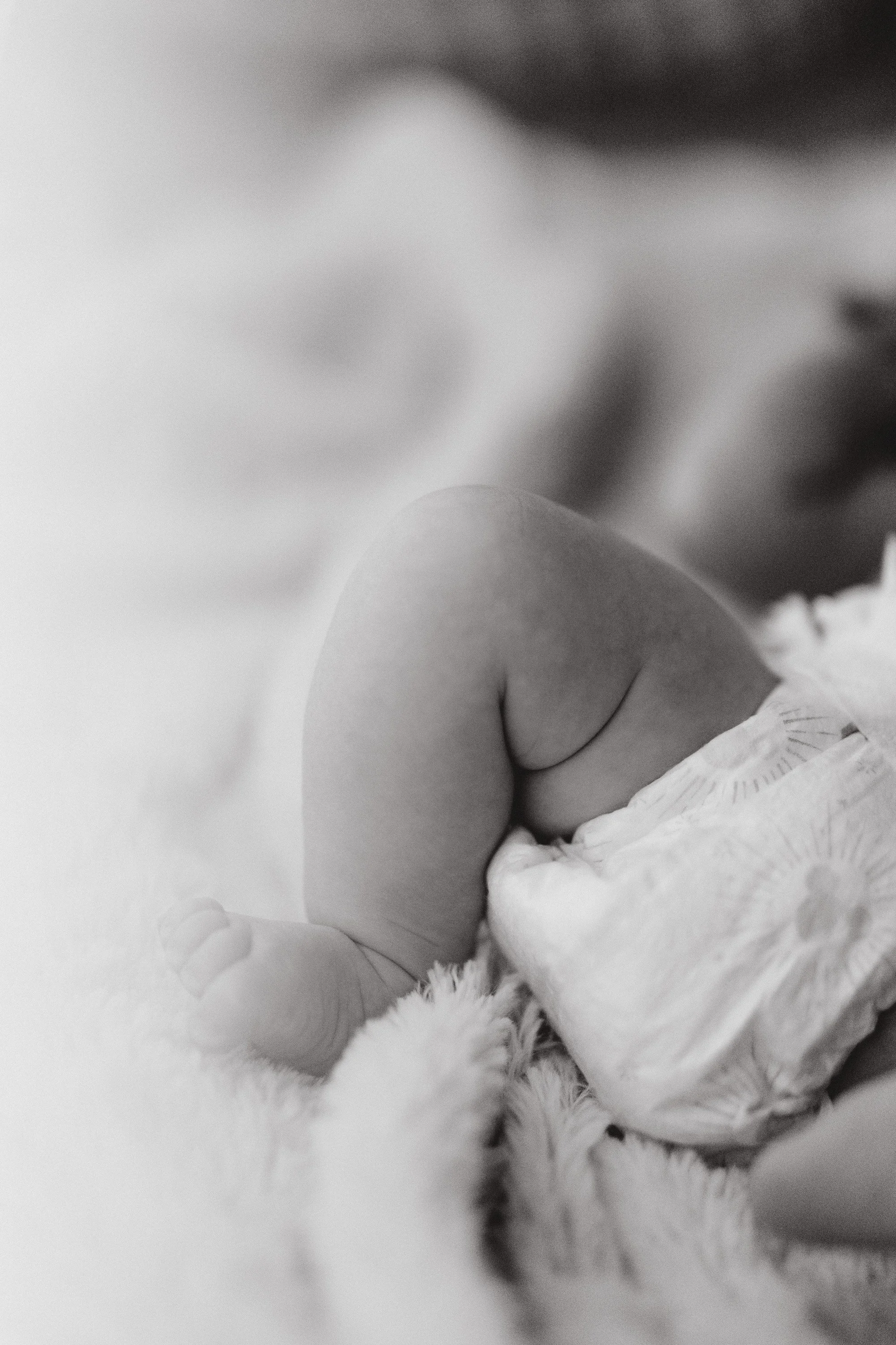 Close-up black and white photo of a baby's face with a focus on the cheek and eye area, with soft textures and gentle lighting.