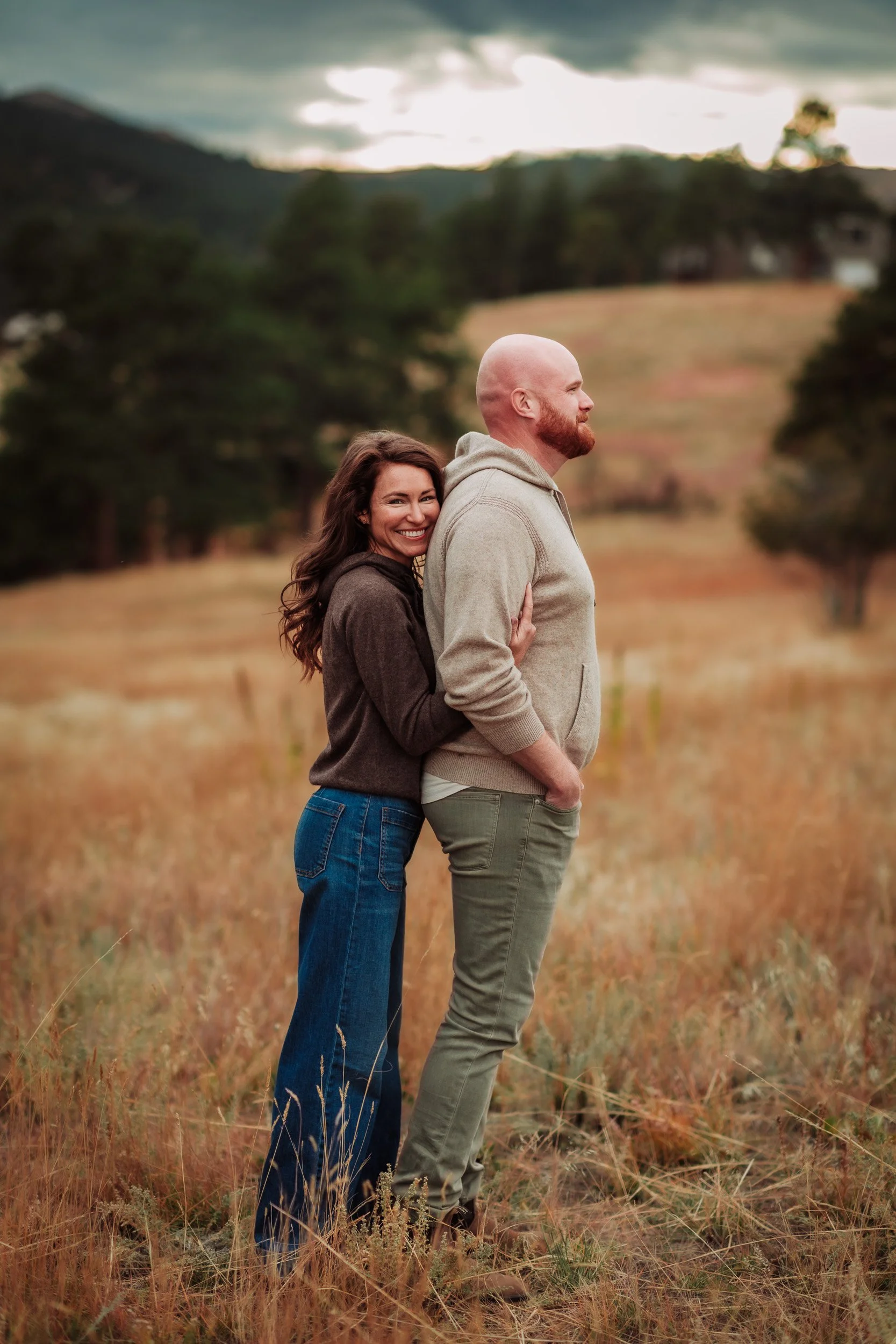 Parents posing among pine trees at Betasso Preserve on a partly cloudy afternoon