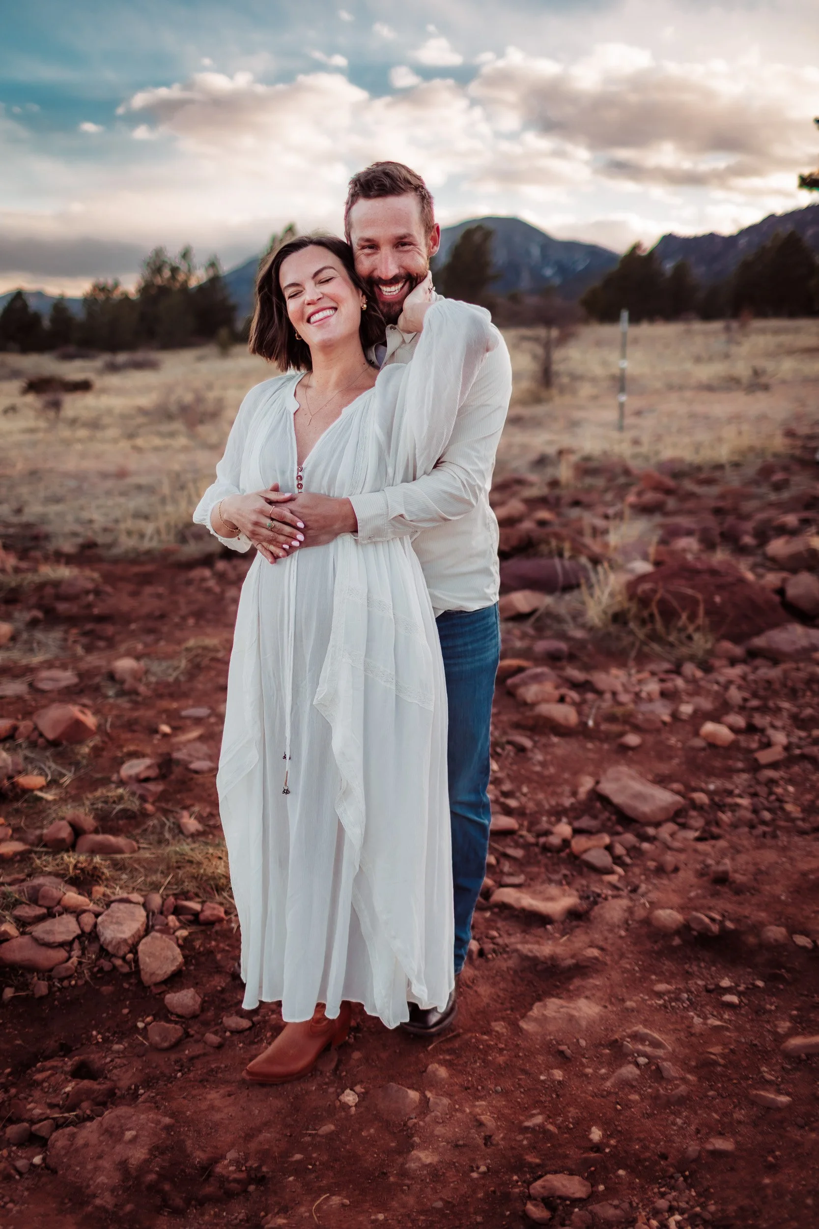 Pregnant woman and partner standing in open field at Shanahan Ridge in Boulder, Colorado during winter golden hour