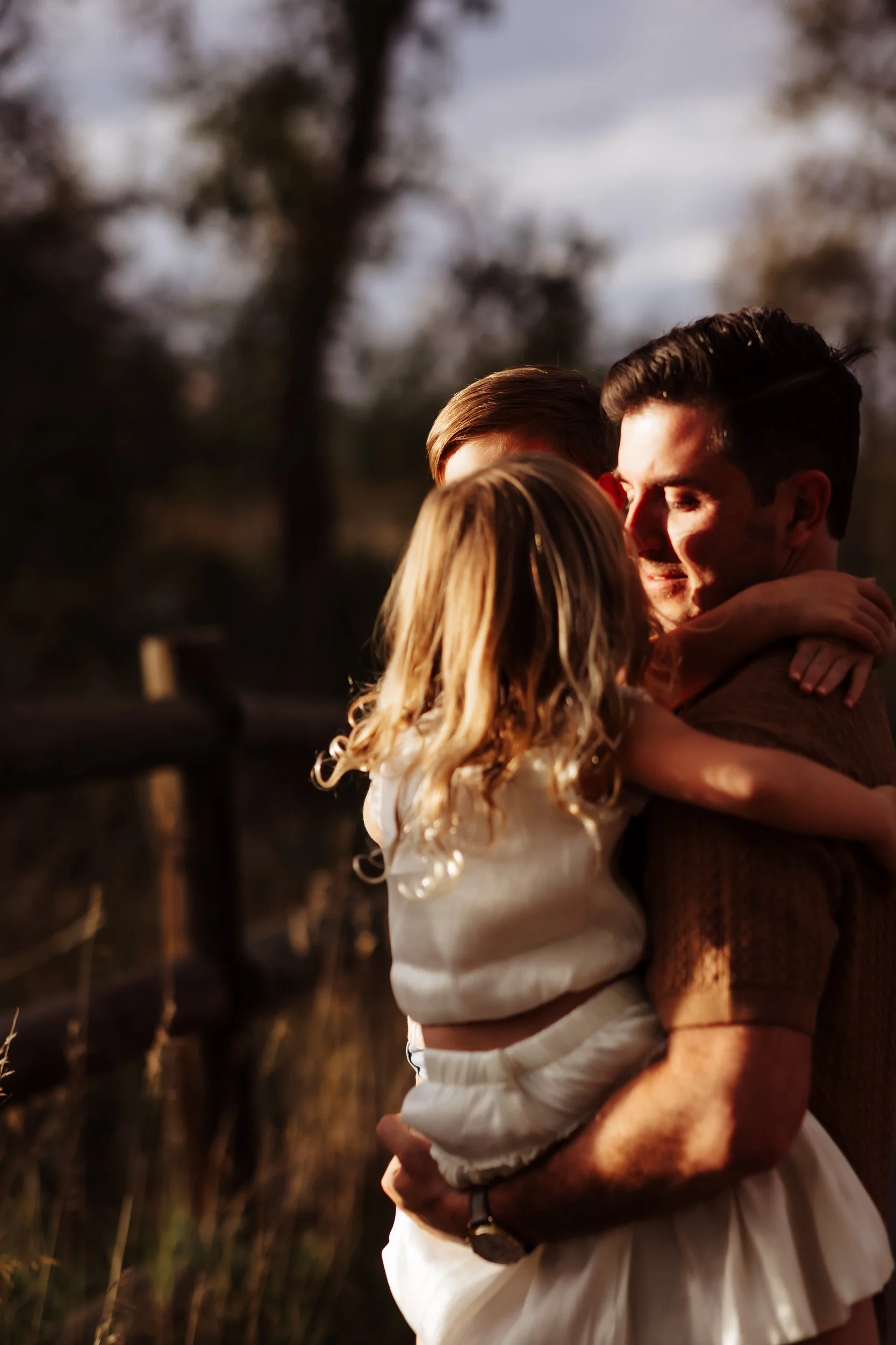 Dad carrying two kids hit by direct golden hour light at South Mesa Trailhead