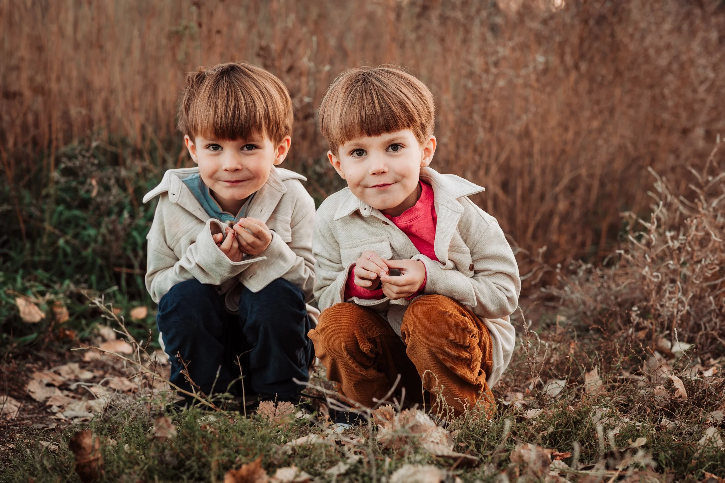 twin boys crouching down in dried grass during fall family photo session in Boulder, CO