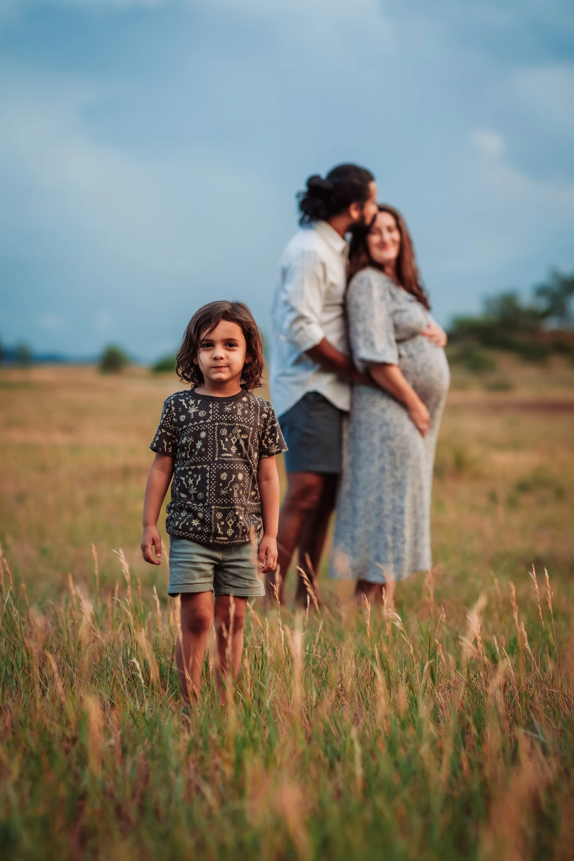 Expecting parents embracing in a field during golden hour
