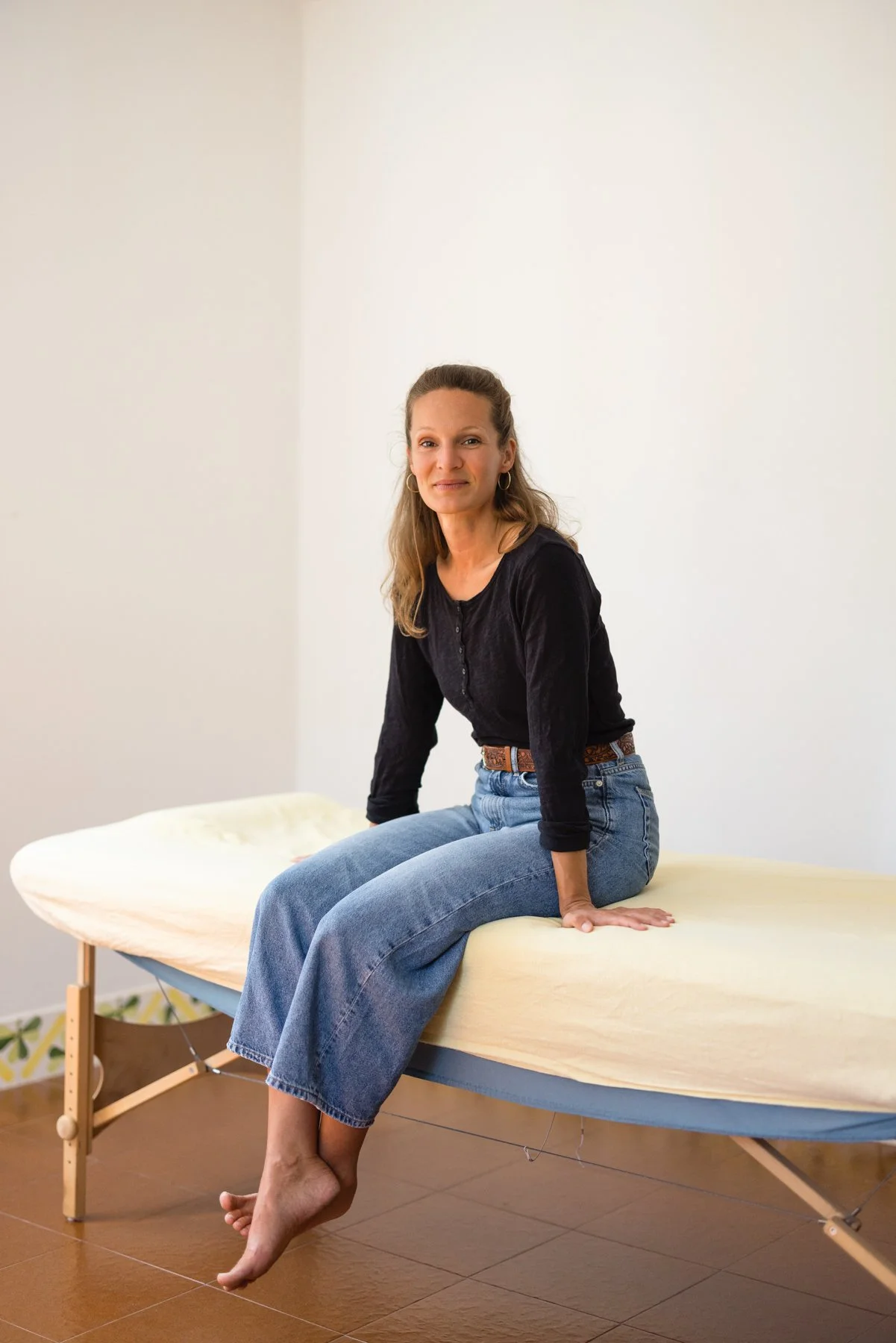 Eine Frau sitzt auf einer Behandlungsliege in einem neutral eingerichteten Raum.