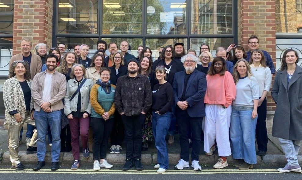 Group of people standing on steps outside a brick building with large windows, posing for a group photo.