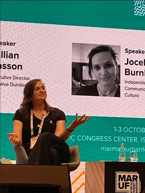 Jocelyn Burnham speaking on stage at the Marmara Urban Forum in Istanbul, October 2025, with her speaker card on the screen behind her.