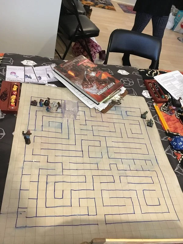 A tabletop maze game with miniatures, dice, rulebooks, and game accessories.