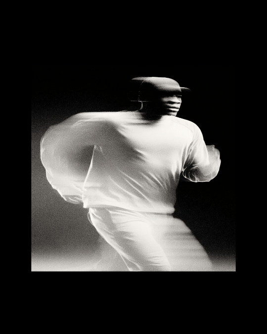 Black and white photo of a person in motion, wearing a light-colored shirt and hat, with motion blur effect.