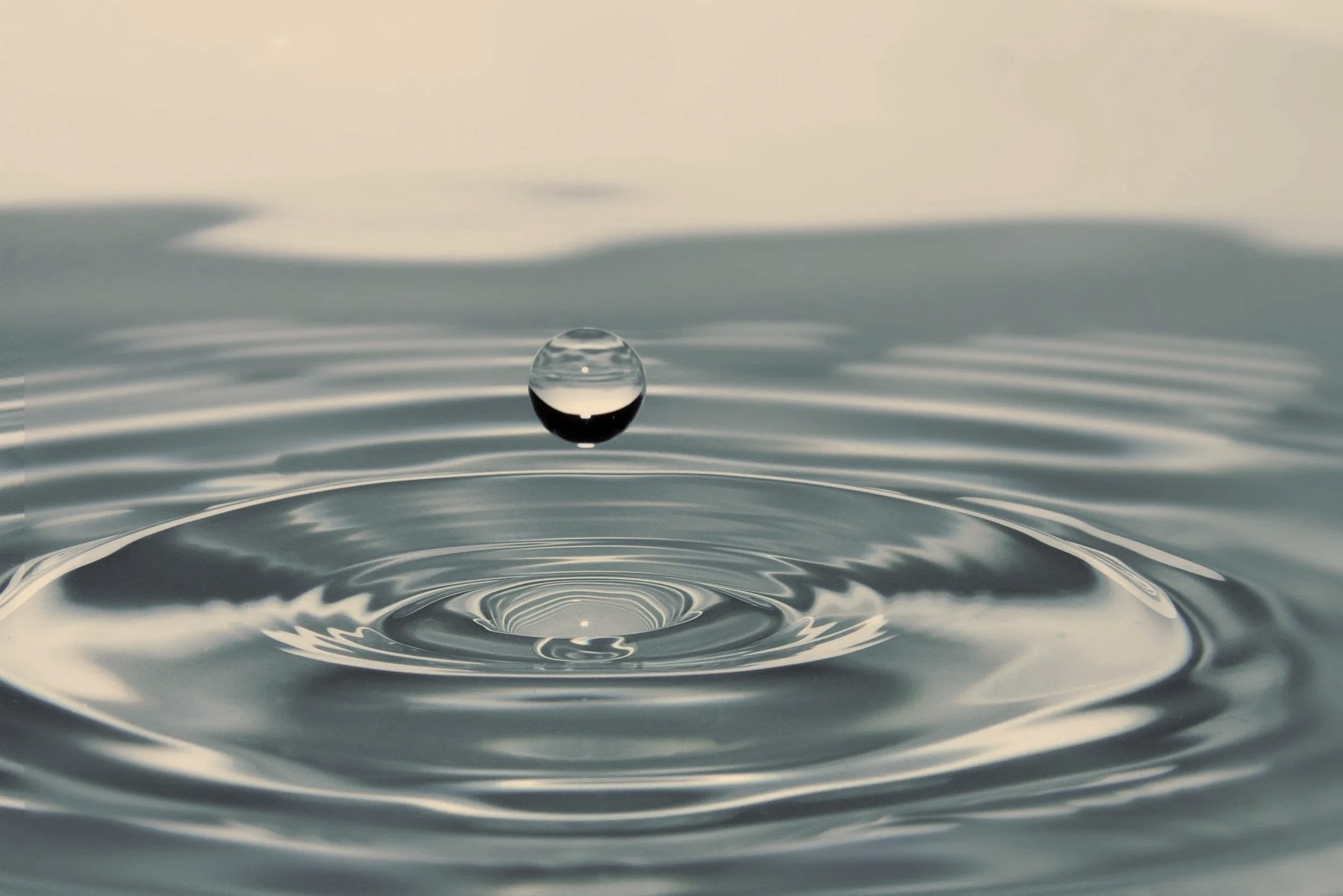 Water droplet creates concentric ripples that spread outward across the surface, symbolizing how trauma can originate from one moment yet have far-reaching effects throughout a person's life.