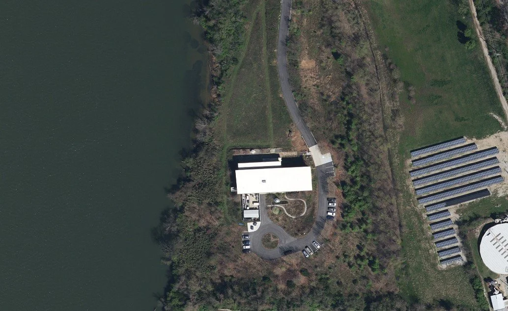Aerial view of a building near a large body of water with parked cars and solar panel arrays.