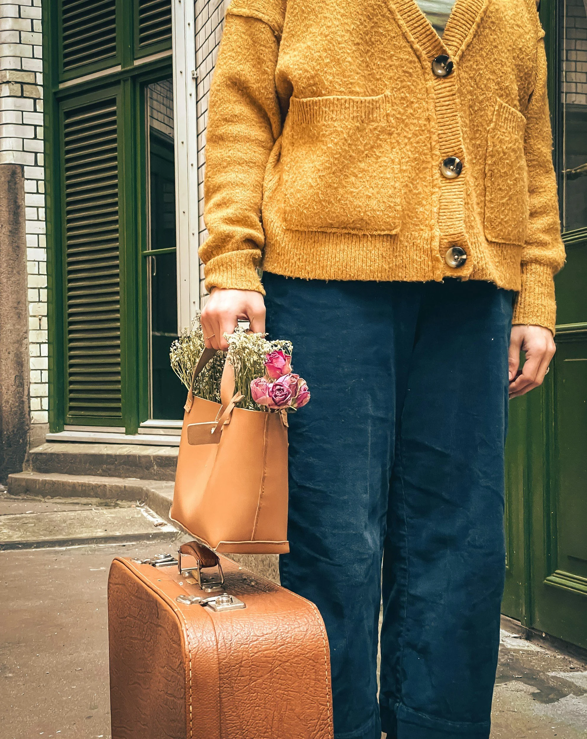 Woman outside of a building with a suitcase and handbag with a bouquet of flowers